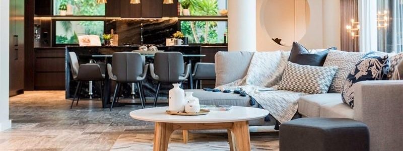 well lit living room with a table and lounge with a dark dining room set and kitchen in the background